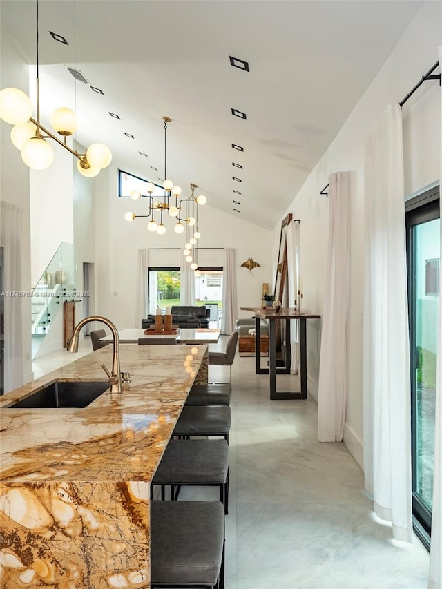 kitchen featuring light stone counters, an inviting chandelier, concrete flooring, pendant lighting, and a sink