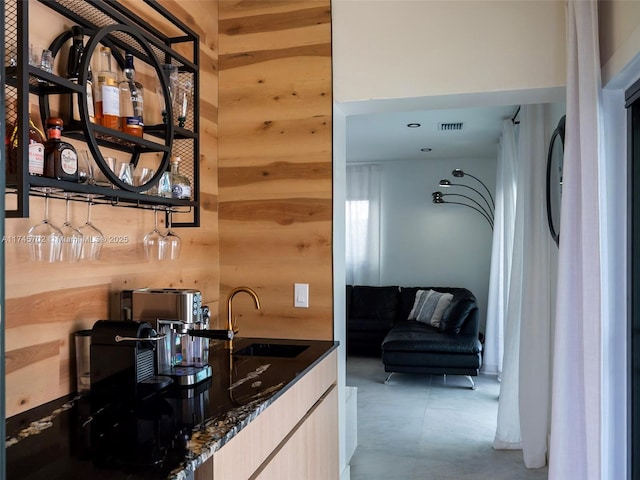 kitchen with visible vents, a sink, wooden walls, dark stone countertops, and modern cabinets