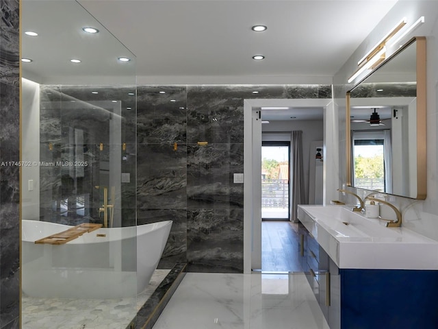 bathroom with a freestanding tub, recessed lighting, vanity, tile walls, and marble finish floor