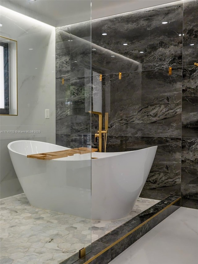 full bath with marble finish floor, a freestanding tub, and tile walls