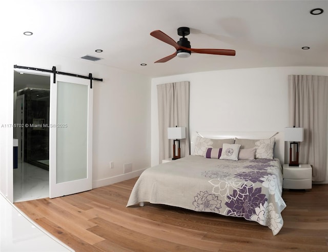 bedroom with recessed lighting, wood finished floors, visible vents, and a barn door