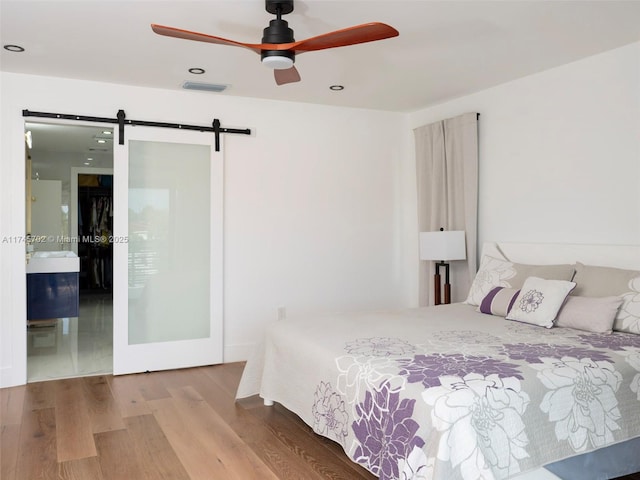 bedroom featuring recessed lighting, visible vents, a barn door, ensuite bath, and wood finished floors