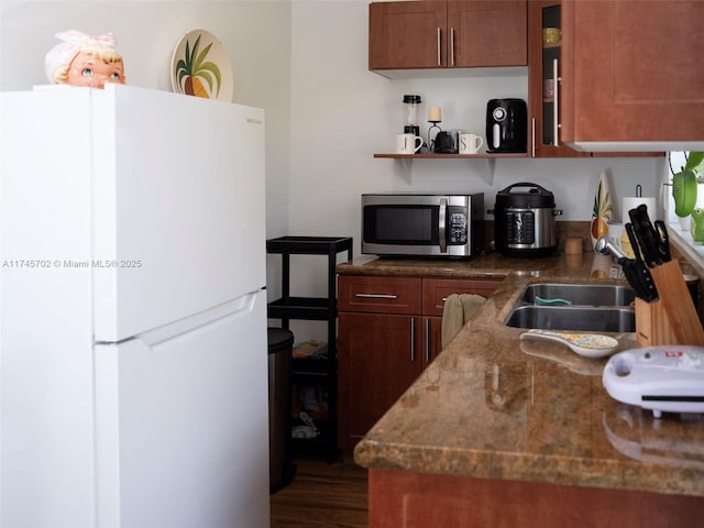 kitchen featuring glass insert cabinets, stainless steel microwave, dark stone countertops, freestanding refrigerator, and a sink