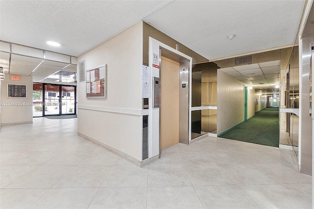 hallway featuring light tile patterned floors, a textured ceiling, a paneled ceiling, and elevator