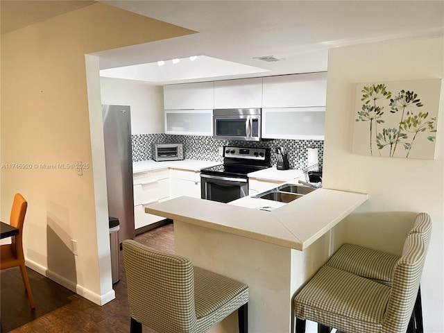 kitchen featuring a kitchen bar, sink, white cabinetry, appliances with stainless steel finishes, and kitchen peninsula