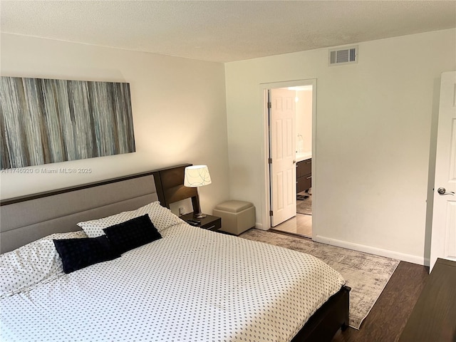 bedroom featuring wood-type flooring, a textured ceiling, and ensuite bath