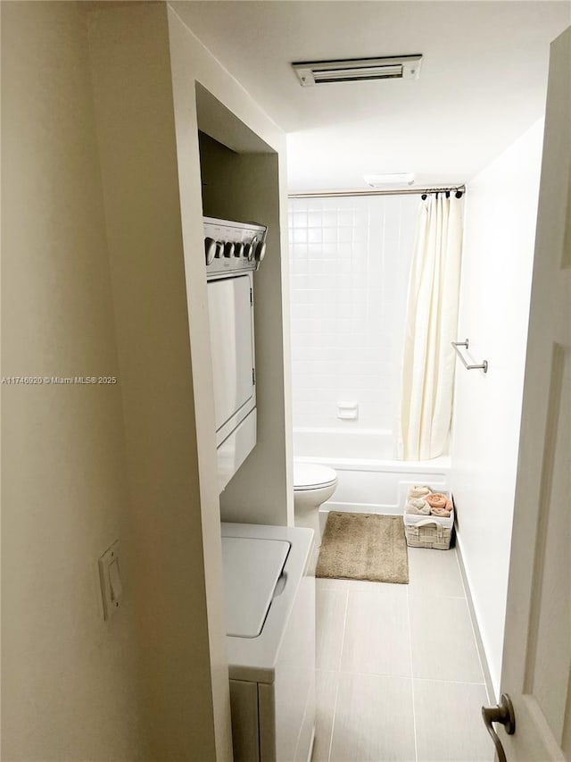 bathroom featuring stacked washer and dryer, toilet, tile patterned flooring, and shower / bath combo with shower curtain