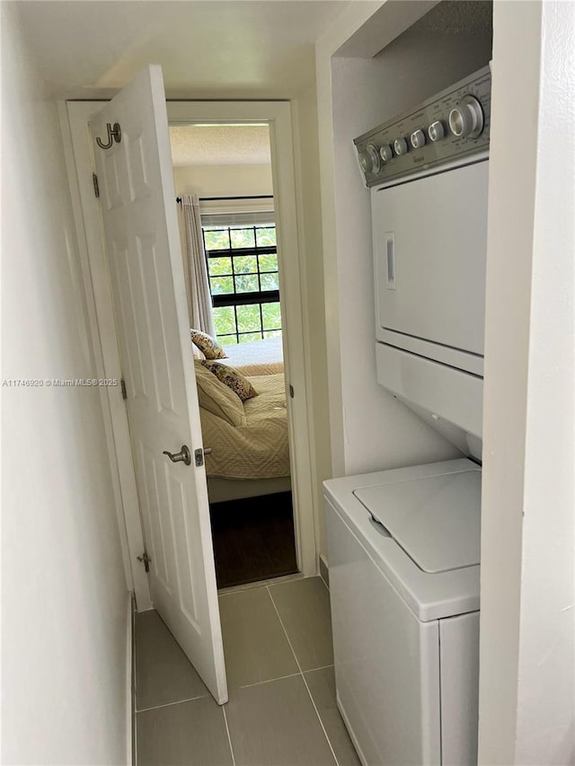 laundry area with stacked washing maching and dryer and light tile patterned floors