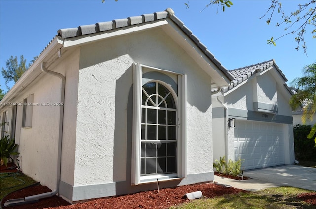 view of side of property featuring stucco siding, a garage, concrete driveway, and a tile roof