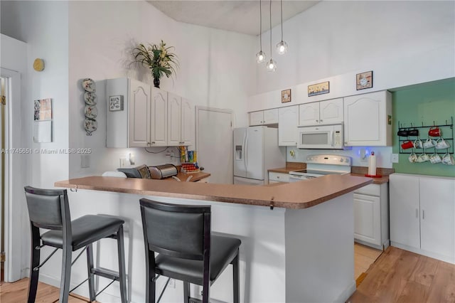 kitchen featuring white appliances, a breakfast bar area, a peninsula, a high ceiling, and white cabinetry