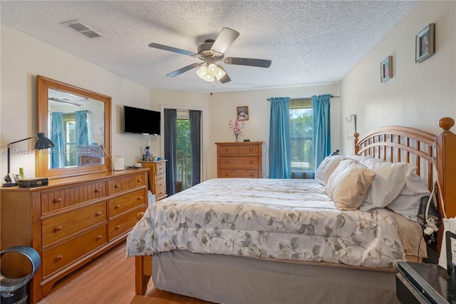 bedroom featuring light wood-style floors, a ceiling fan, visible vents, and a textured ceiling