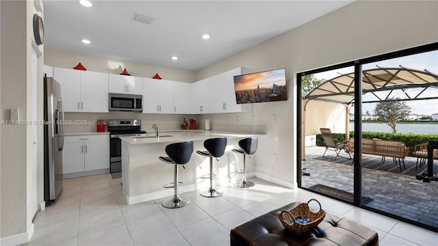 kitchen with sink, a breakfast bar area, light tile patterned floors, stainless steel appliances, and white cabinets