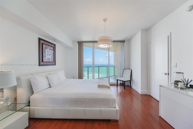 bedroom featuring a water view, dark hardwood / wood-style floors, a textured ceiling, and a wall of windows