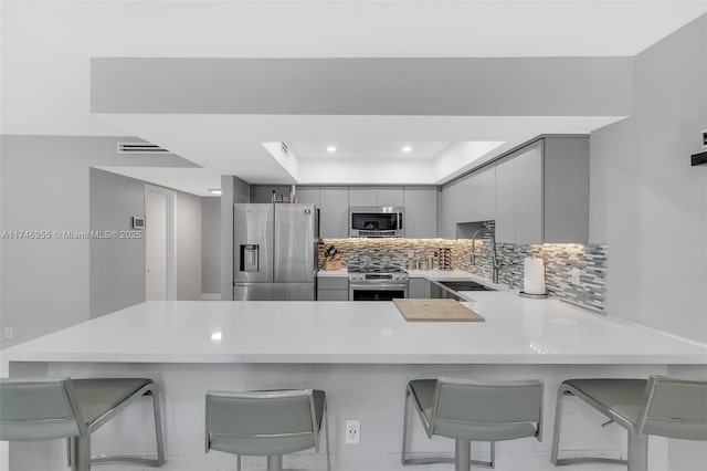 kitchen featuring kitchen peninsula, stainless steel appliances, a breakfast bar, sink, and gray cabinets