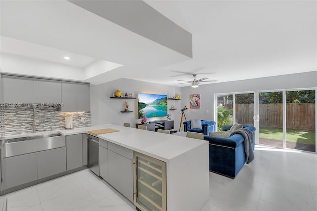 kitchen featuring beverage cooler, backsplash, gray cabinets, sink, and kitchen peninsula