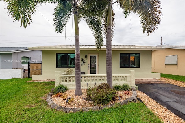 ranch-style house with stucco siding, a front yard, a standing seam roof, metal roof, and fence