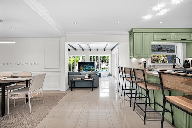 kitchen with a healthy amount of sunlight, green cabinetry, beamed ceiling, and a kitchen bar