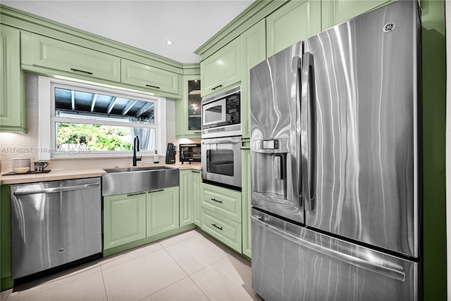 kitchen featuring light tile patterned floors, appliances with stainless steel finishes, a sink, and green cabinets