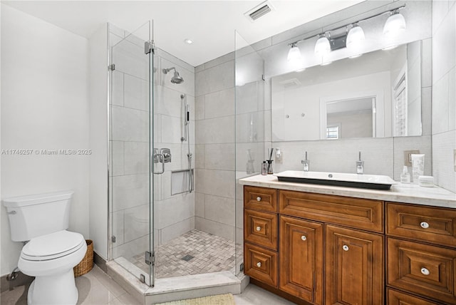 bathroom featuring toilet, vanity, visible vents, a shower stall, and tasteful backsplash