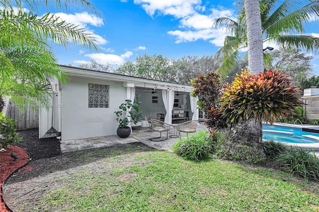 rear view of property featuring fence, a ceiling fan, a lawn, stucco siding, and a patio area