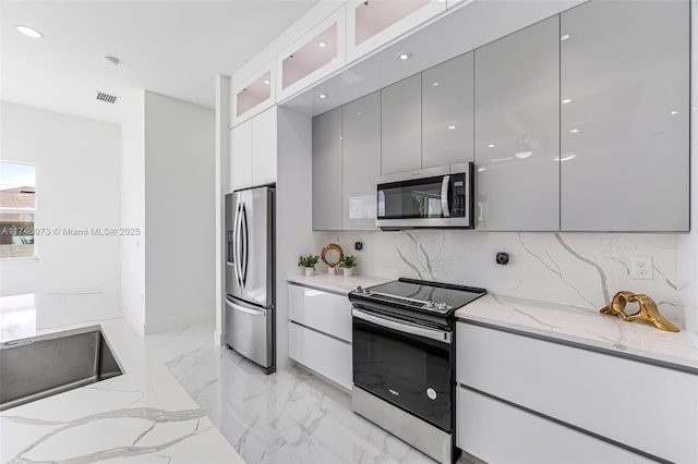 kitchen featuring tasteful backsplash, appliances with stainless steel finishes, light stone countertops, and gray cabinetry