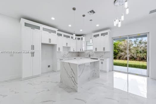 kitchen with white cabinetry, a center island, pendant lighting, and light stone counters