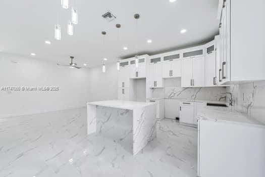 kitchen with a kitchen island, white cabinetry, sink, hanging light fixtures, and light stone counters