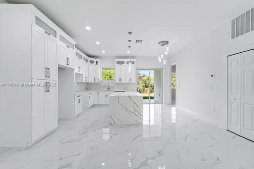 kitchen featuring hanging light fixtures, light stone countertops, a center island, and white cabinets