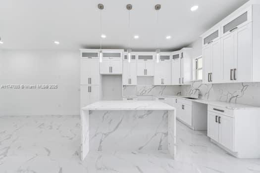 kitchen with a center island, white cabinets, light stone counters, and decorative light fixtures