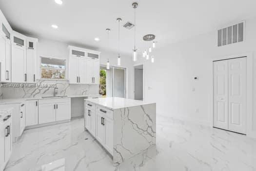 kitchen featuring a kitchen island, pendant lighting, white cabinetry, sink, and light stone countertops