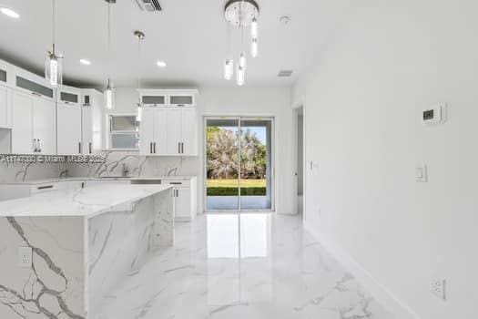 kitchen featuring light stone counters, white cabinetry, and decorative light fixtures