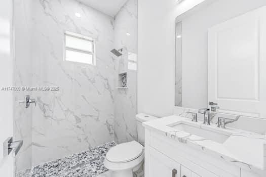 bathroom featuring tiled shower, vanity, and toilet