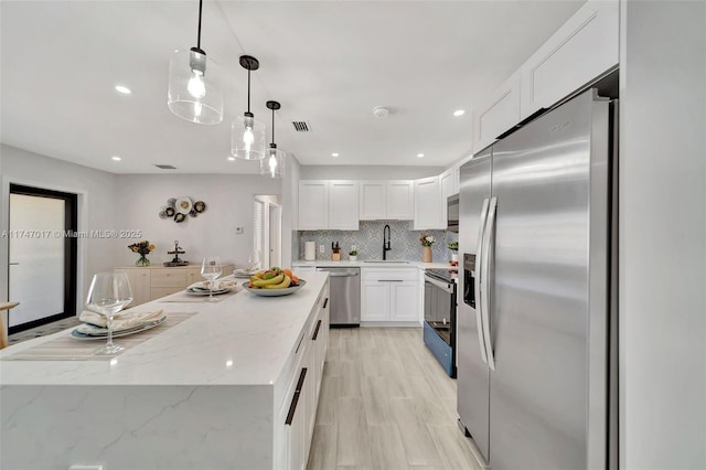 kitchen with sink, white cabinetry, hanging light fixtures, stainless steel appliances, and decorative backsplash