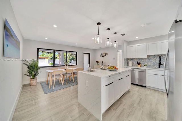 kitchen with decorative light fixtures, a center island, white cabinets, and appliances with stainless steel finishes