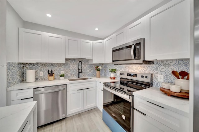 kitchen with white cabinetry, sink, backsplash, stainless steel appliances, and light stone countertops