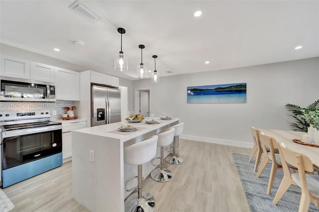 kitchen with appliances with stainless steel finishes, pendant lighting, tasteful backsplash, white cabinetry, and a center island