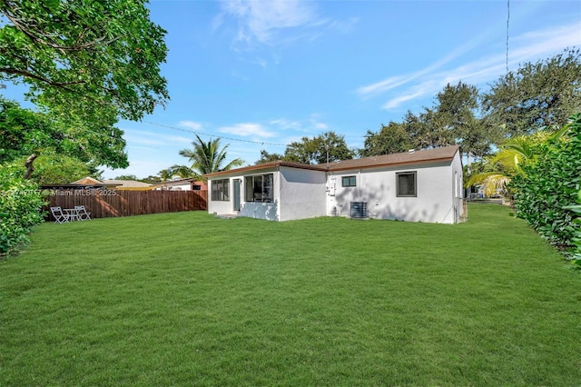 rear view of house with central AC and a lawn