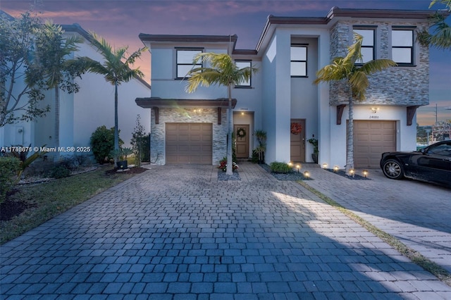 view of front of home featuring a garage, stone siding, decorative driveway, and stucco siding