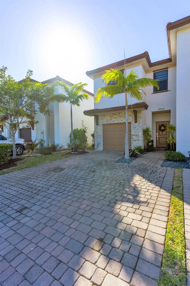 view of front of house featuring stone siding, decorative driveway, a garage, and stucco siding