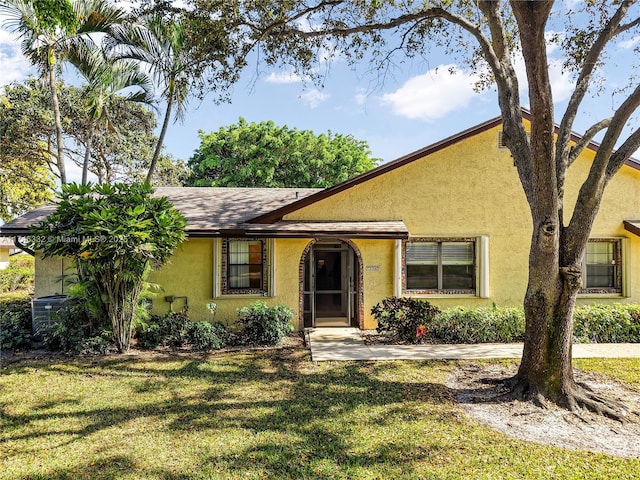 view of front facade featuring roof with shingles, central AC unit, a front lawn, and stucco siding