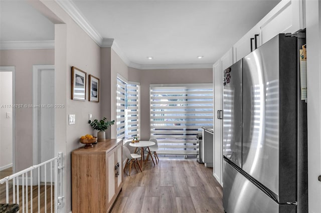 interior space featuring light wood-type flooring, wooden counters, crown molding, stainless steel fridge, and white cabinets