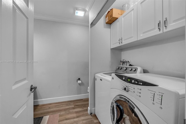 clothes washing area with ornamental molding, cabinets, washing machine and clothes dryer, and light hardwood / wood-style flooring