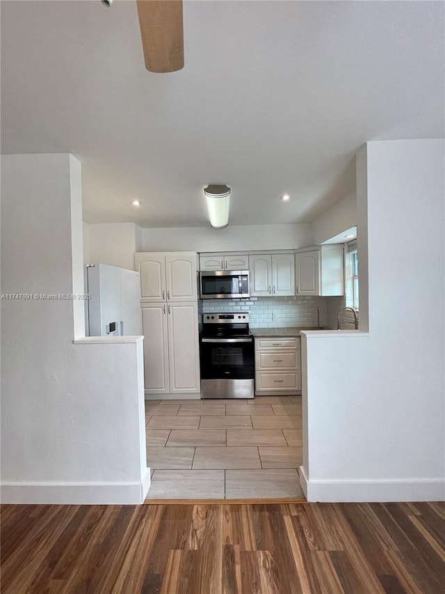 kitchen with white cabinetry, light wood-type flooring, kitchen peninsula, stainless steel appliances, and backsplash