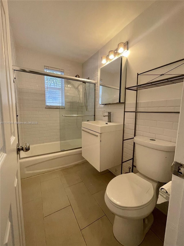 full bathroom with tile patterned flooring, toilet, tile walls, vanity, and bath / shower combo with glass door