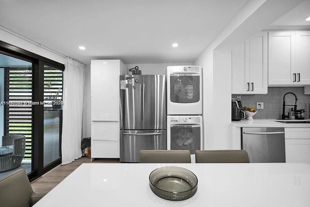 kitchen featuring tasteful backsplash, stacked washer / dryer, stainless steel appliances, sink, and white cabinetry