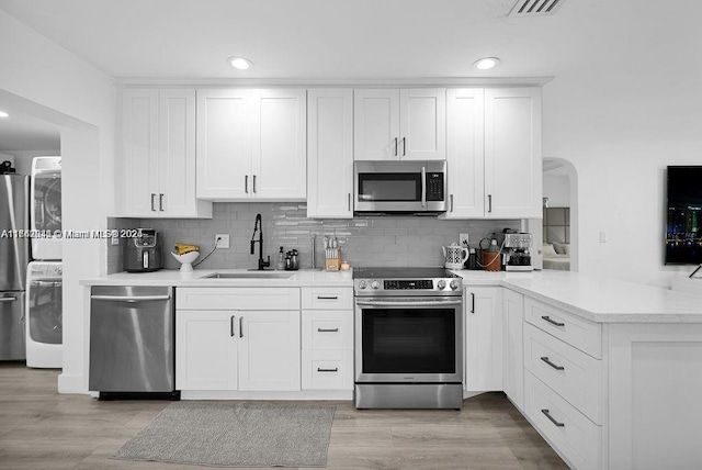 kitchen with appliances with stainless steel finishes, stacked washer and dryer, and white cabinets