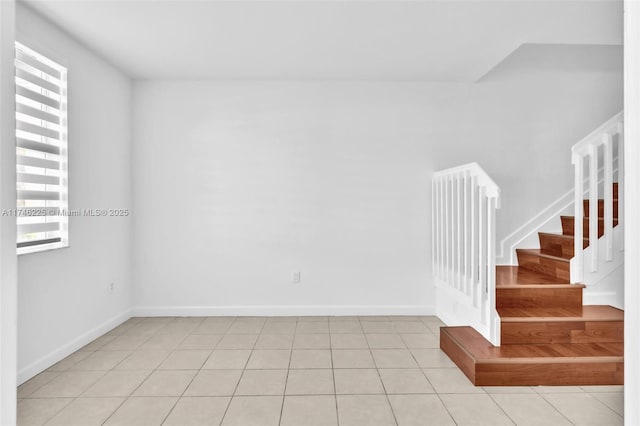 empty room featuring light tile patterned floors, baseboards, and stairs
