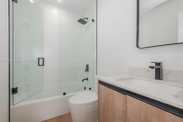 full bathroom featuring hardwood / wood-style flooring, bath / shower combo with glass door, vanity, and toilet