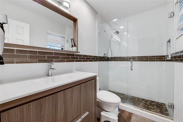 bathroom featuring tile walls, a shower stall, toilet, and vanity