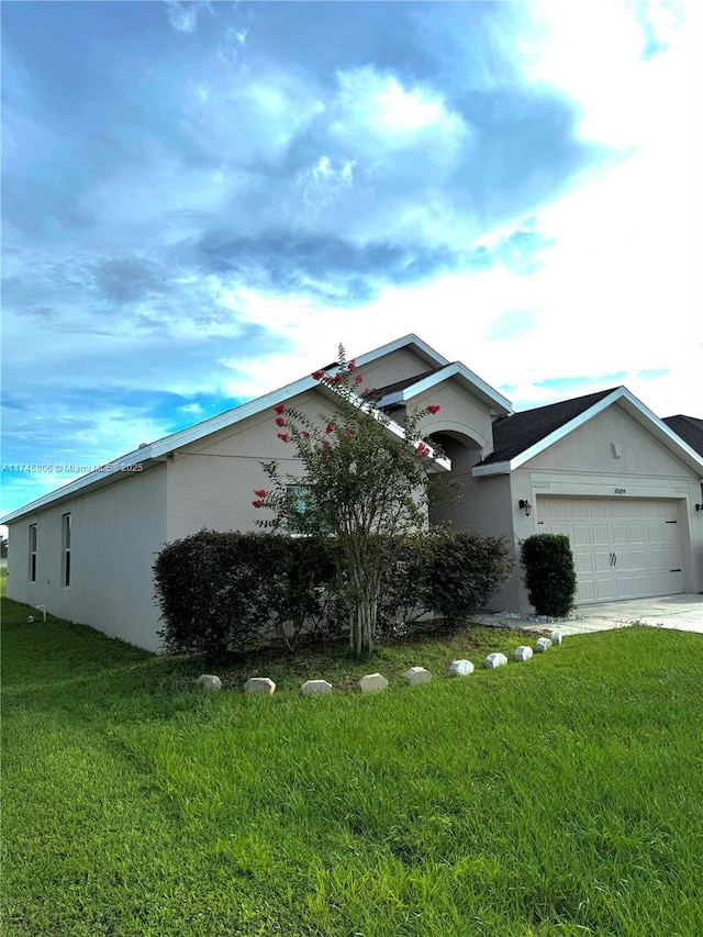 exterior space featuring a garage, driveway, a front lawn, and stucco siding